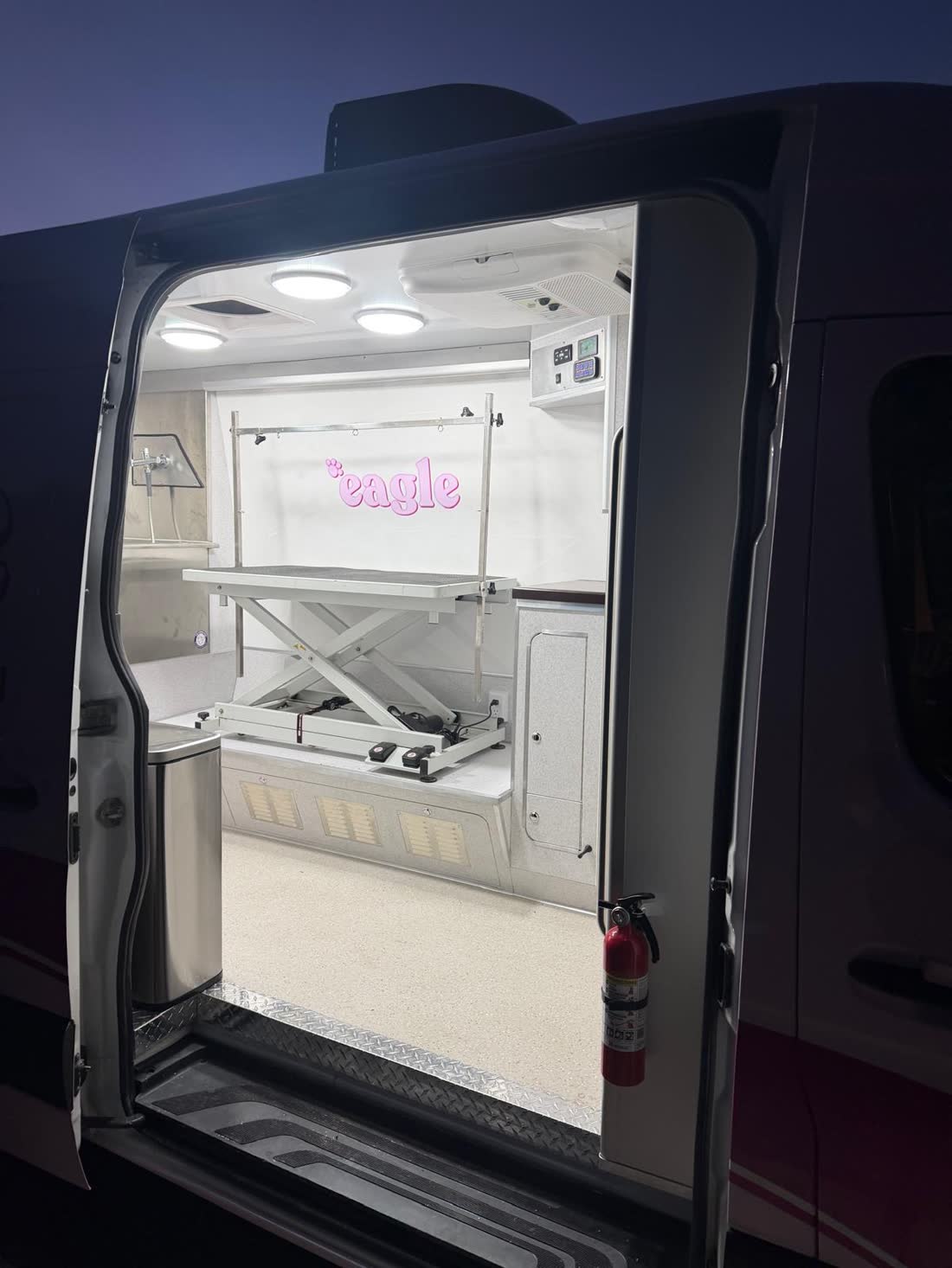 Sliding door open at dusk showing the lit grooming room, lift table and vented dryer platform